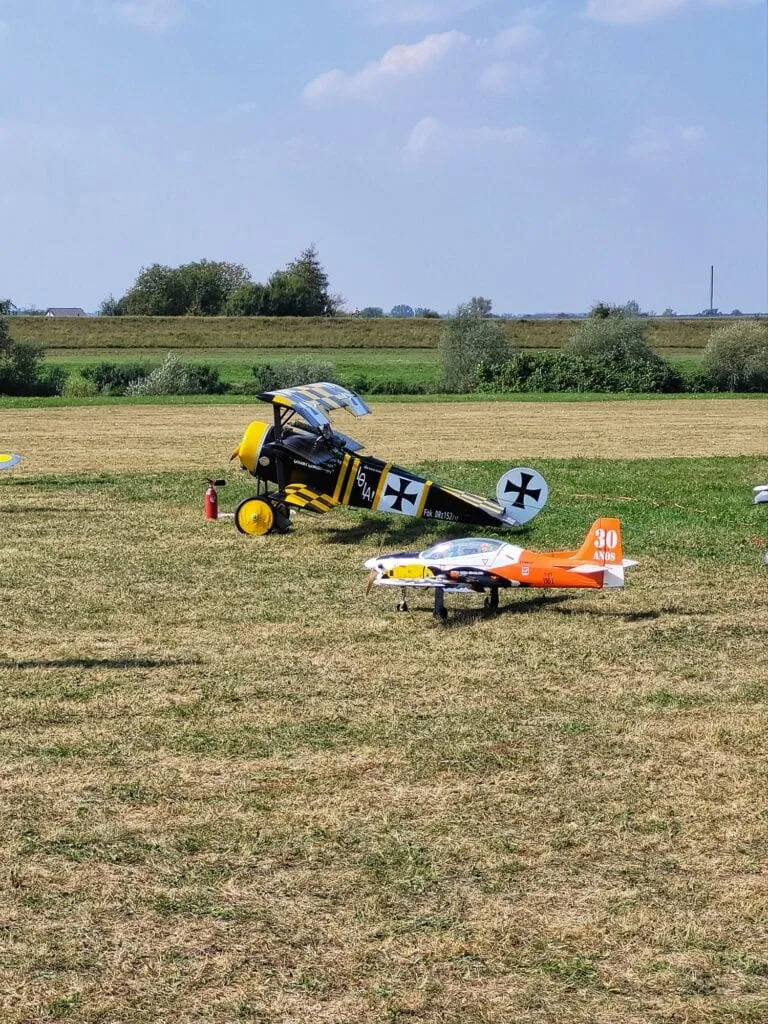 Czarno-żółty model dwupłata z krzyżem maltańskim i pomarańczowo-biały model odrzutowca na trawiastym pasie